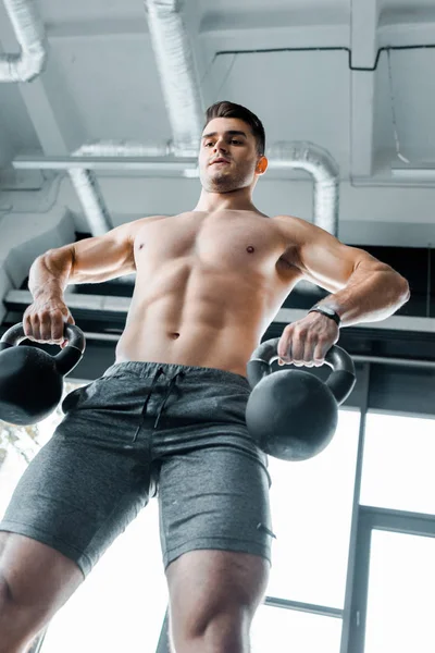 Vista de ángulo bajo del deportista guapo y sin camisa haciendo ejercicio con pesas en el centro deportivo - foto de stock