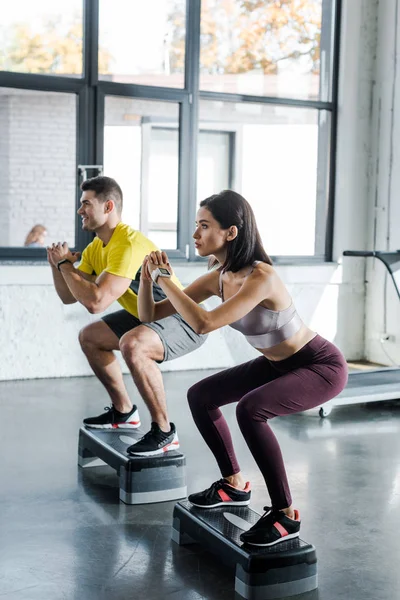 Sportsman and sportswoman doing squat on step platforms in sports center — Stock Photo