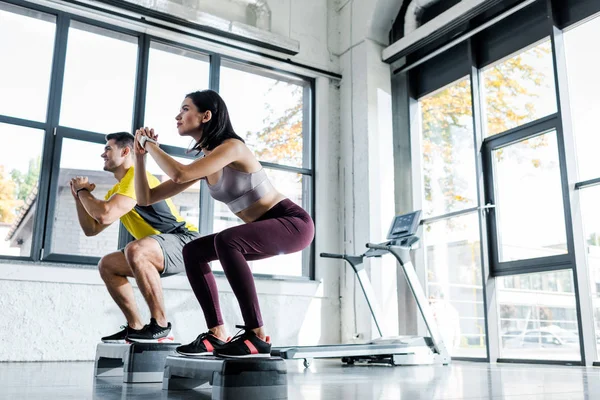 Sportsman and sportswoman doing squat on step platforms in sports center — Stock Photo