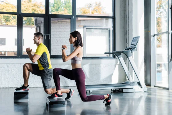 Side view of handsome sportsman and sportswoman doing lunges on step platforms in sports center — Stock Photo