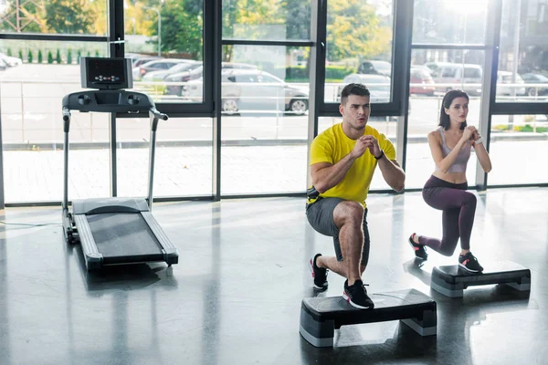 Handsome sportsman and sportswoman doing lunges on step platforms in sports center — Stock Photo