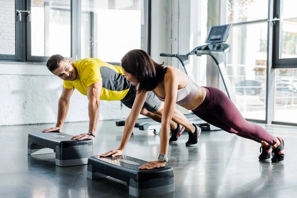 Handsome sportsman and sportswoman doing plank on step platforms in sports center — Stock Photo