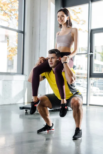 Sportsman squatting and holding sportswoman on shoulders in sports center — Stock Photo