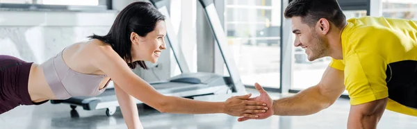 Panoramic shot of smiling sportsman and sportswoman doing plank and clapping in sports center — Stock Photo