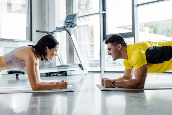 Smiling sportsman and sportswoman doing plank and clapping on fitness mats in sports center — Stock Photo