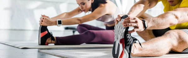 Panoramic shot of sportsman and sportswoman stretching on fitness mats in sports center — Stock Photo