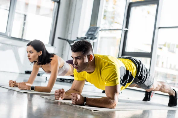 Sportsman e sportswoman che fanno asse su stuoie di idoneità in centro sportivo — Foto stock