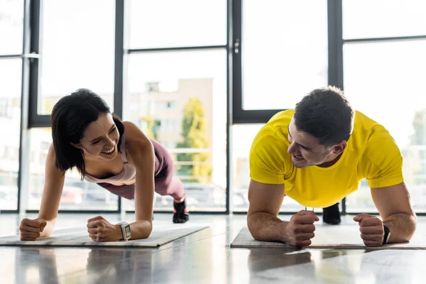 Smiling sportsman and sportswoman doing plank on fitness mats in sports center — Stock Photo