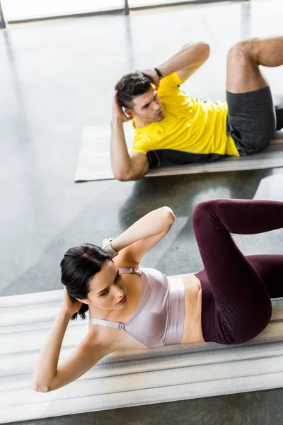 Sportsman and sportswoman doing crunches on fitness mats in sports center — Stock Photo