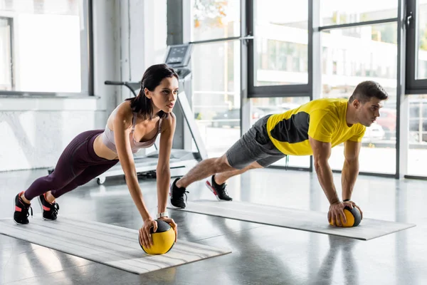 Sportsman and sportswoman doing plank with balls in sports center — Stock Photo