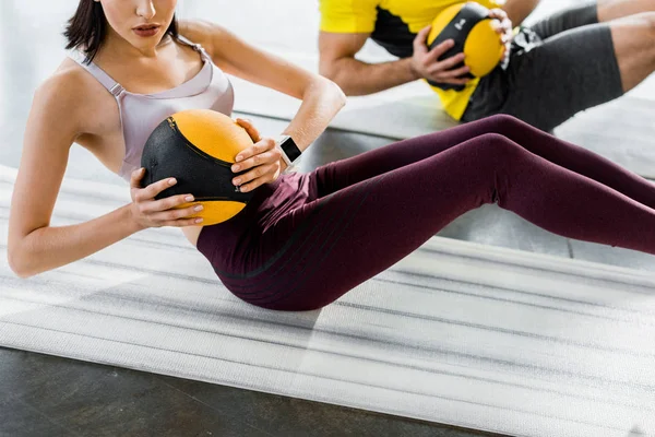 Vista recortada de deportista y deportista haciendo crujidos con bolas en colchonetas de fitness en el centro deportivo - foto de stock