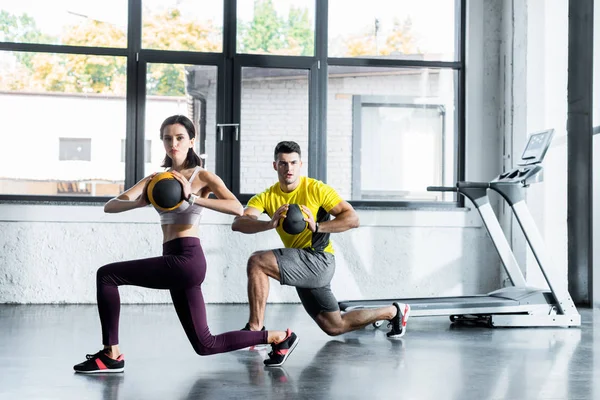 Sportsman and sportswoman doing lunges with balls in sports center — Stock Photo