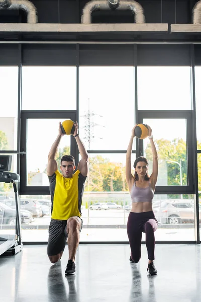 Sportsman and sportswoman doing lunges with balls in sports center — Stock Photo