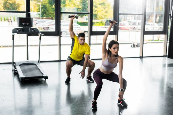 Sportsman and sportswoman doing squat with dumbbells in sports center — Stock Photo