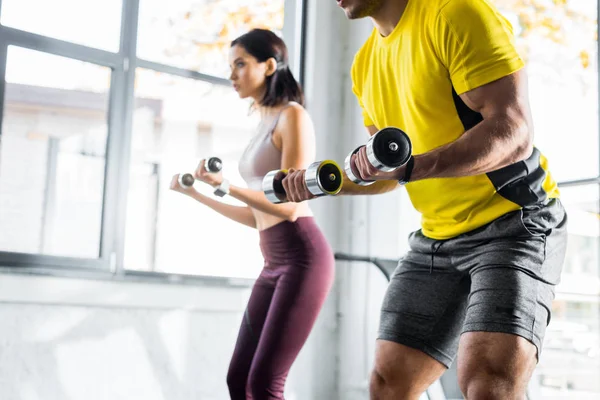 Cropped view of sportsman and sportswoman working out with dumbbells in sports center — Stock Photo