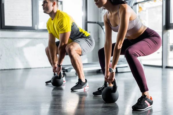 Cropped view of sportsman and sportswoman doing squat with weights in sports center — Stock Photo