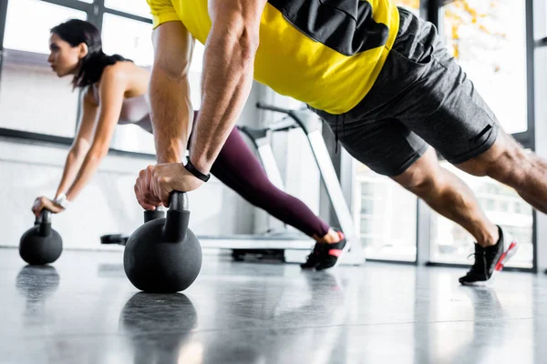 Cropped view of sportsman and sportswoman doing plank on weights in sports center — Stock Photo