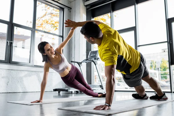 Desportista e sorrindo desportista fazendo prancha e batendo palmas em tapetes de fitness no centro de esportes — Fotografia de Stock