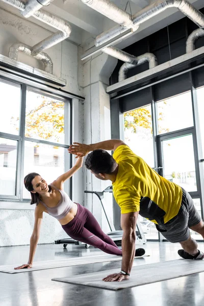 Deportista y deportista sonriente haciendo tablón y aplaudiendo en colchonetas de fitness en el centro deportivo - foto de stock