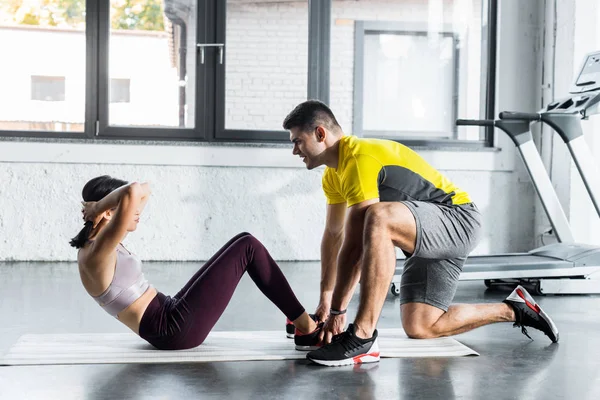 Deportista haciendo abdominales y deportista ayudándola en centro deportivo - foto de stock