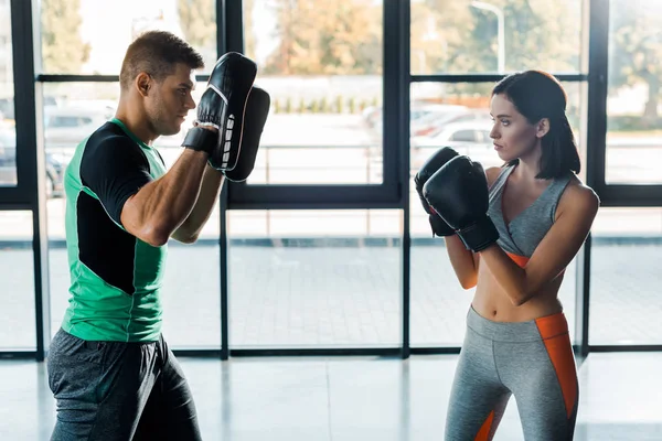 Sportswoman in boxing gloves working out with sportsman in sports center — Stock Photo