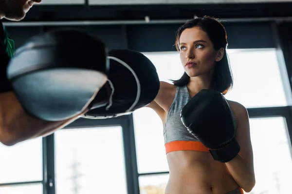 Sportswoman in boxing gloves working out with sportsman in sports center — Stock Photo