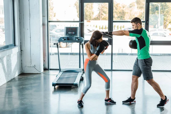 Спортсменка в боксёрских перчатках тренируется со спортсменкой в спорткомплексе — стоковое фото