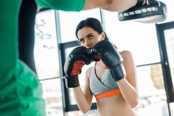 Спортсменка в боксёрских перчатках тренируется со спортсменкой в спорткомплексе — стоковое фото
