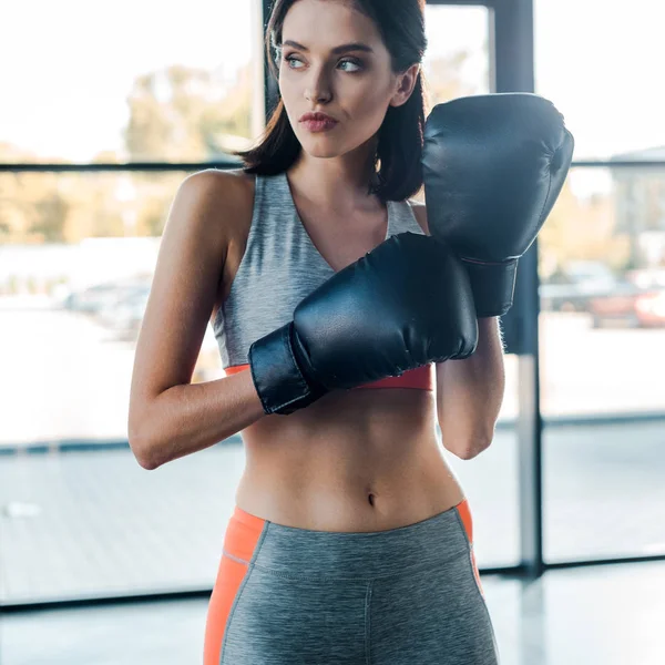 Спортсменка в боксерских перчатках, смотрящая в сторону в спорткомплексе — стоковое фото