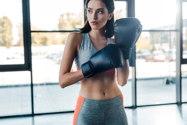 Sportswoman in boxing gloves looking away in sports center — Stock Photo