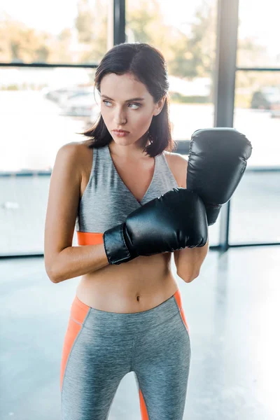 Deportista en guantes de boxeo mirando hacia otro lado en el centro deportivo - foto de stock