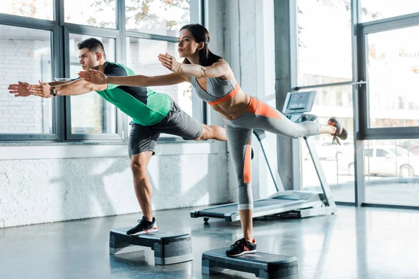 Sportsman and sportswoman working out on step platforms in sports center — Stock Photo