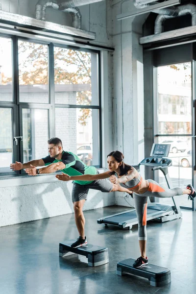 Sportsman and sportswoman working out on step platforms in sports center — Stock Photo