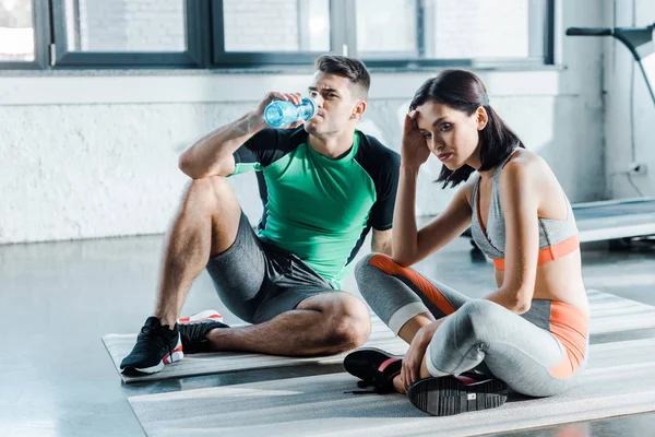 Sportsman drinking water and sportswoman sitting in sports center — Stock Photo