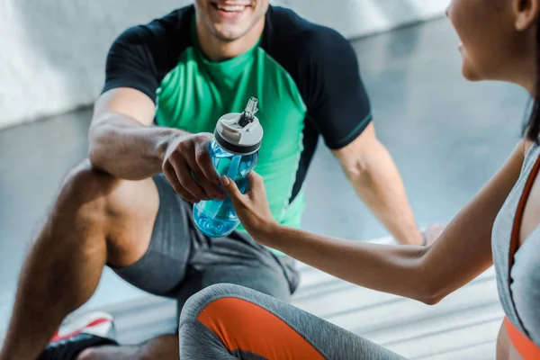 Vista cortada de desportista sorrindo dando garrafa de esportes para desportista no centro de esportes — Fotografia de Stock