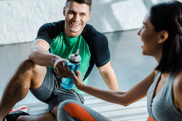 Smiling sportsman giving sports bottle to sportswoman in sports center — Stock Photo