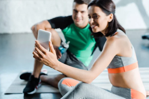 Selective focus of sportswoman taking selfie with sportsman in sports center — Stock Photo