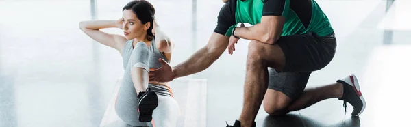 Plano panorámico de la deportista haciendo abdominales y deportista ayudándola en el centro deportivo - foto de stock