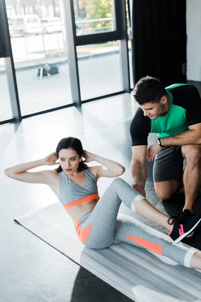 Sportswoman doing crunches and sportsman helping her in sports center — Stock Photo