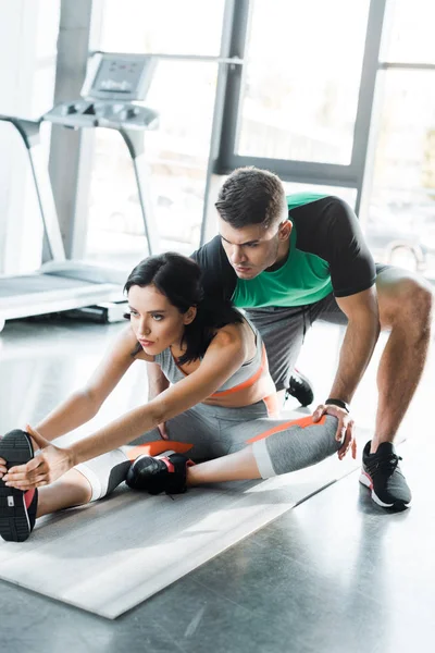 Sportswoman stretching and sportsman helping her in sports center — Stock Photo