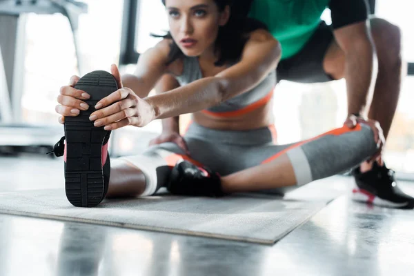 Selective focus of sportswoman stretching and sportsman helping her in sports center — Stock Photo
