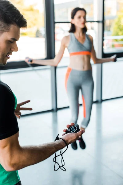 Selektiver Fokus der Sportlerin beim Springen mit Springseil und Sportler mit Stoppuhr — Stockfoto