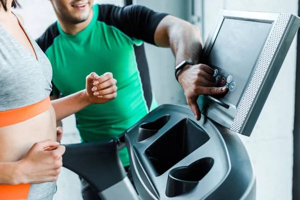 Cropped view of sportswoman running on treadmill and sportsman pointing with finger — Stock Photo