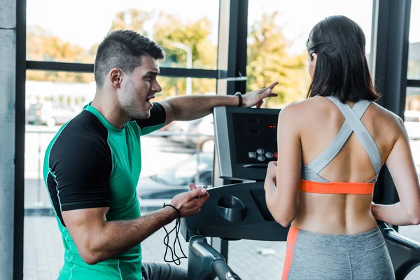 Back view of sportswoman running on treadmill and sportsman standing near — Stock Photo