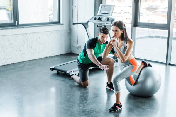 Sportswoman doing lunges on fitness ball and sportsman help her — Stock Photo