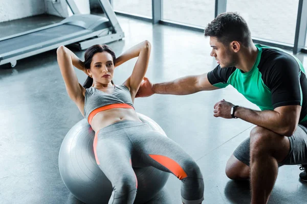 Sportswoman doing crunches on fitness ball and sportsman help her — Stock Photo