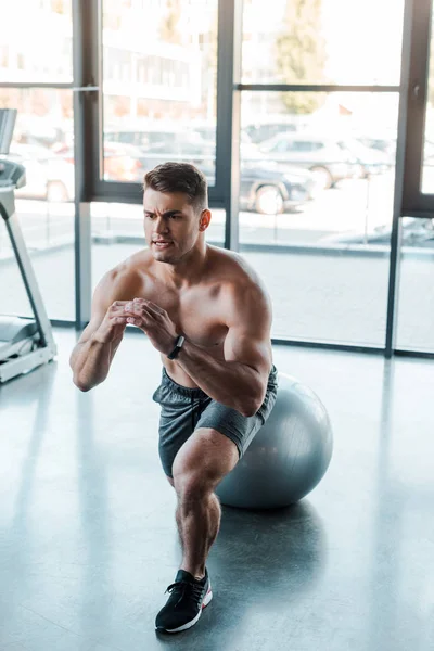 Handsome sportsman doing lunges on fitness ball in sports center — Stock Photo
