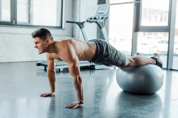 Desportista bonito fazendo prancha na bola de fitness no centro de esportes — Fotografia de Stock