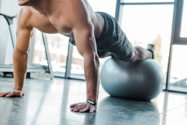 Vista ritagliata di bello sportivo che fa tavola sulla palla fitness nel centro sportivo — Foto stock