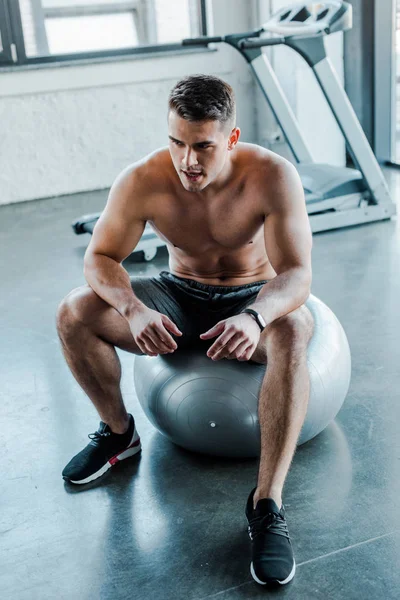 Handsome sportsman sitting on fitness ball in sports center — Stock Photo